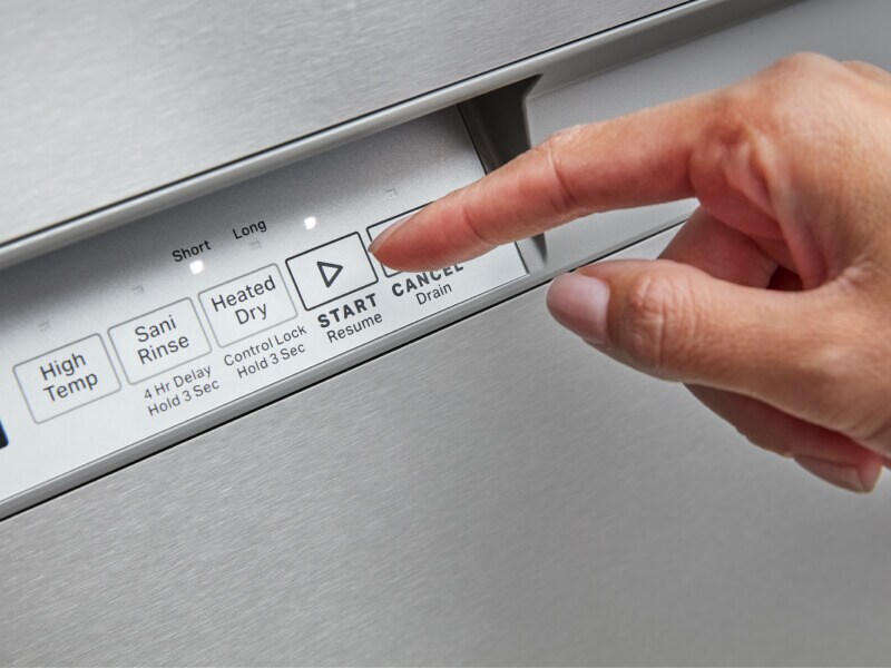 A finger pushing the start button of a dishwasher control panel