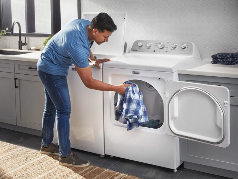 A person adding a blue and white shirt to a dryer A person adding a blue and white shirt to a dryer