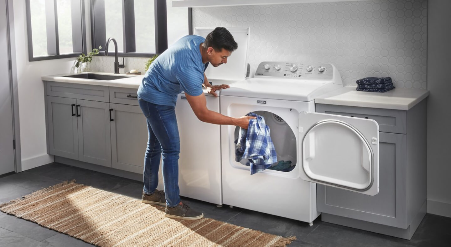 A person adding a blue and white shirt to a dryer A person adding a blue and white shirt to a dryer