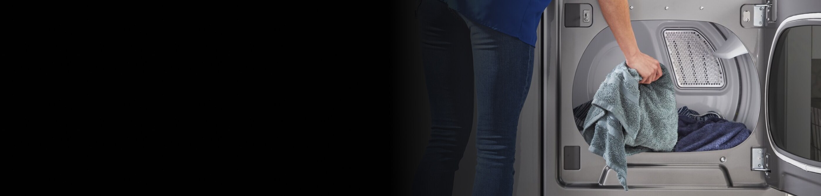 A person placing a blue towel into a dryer