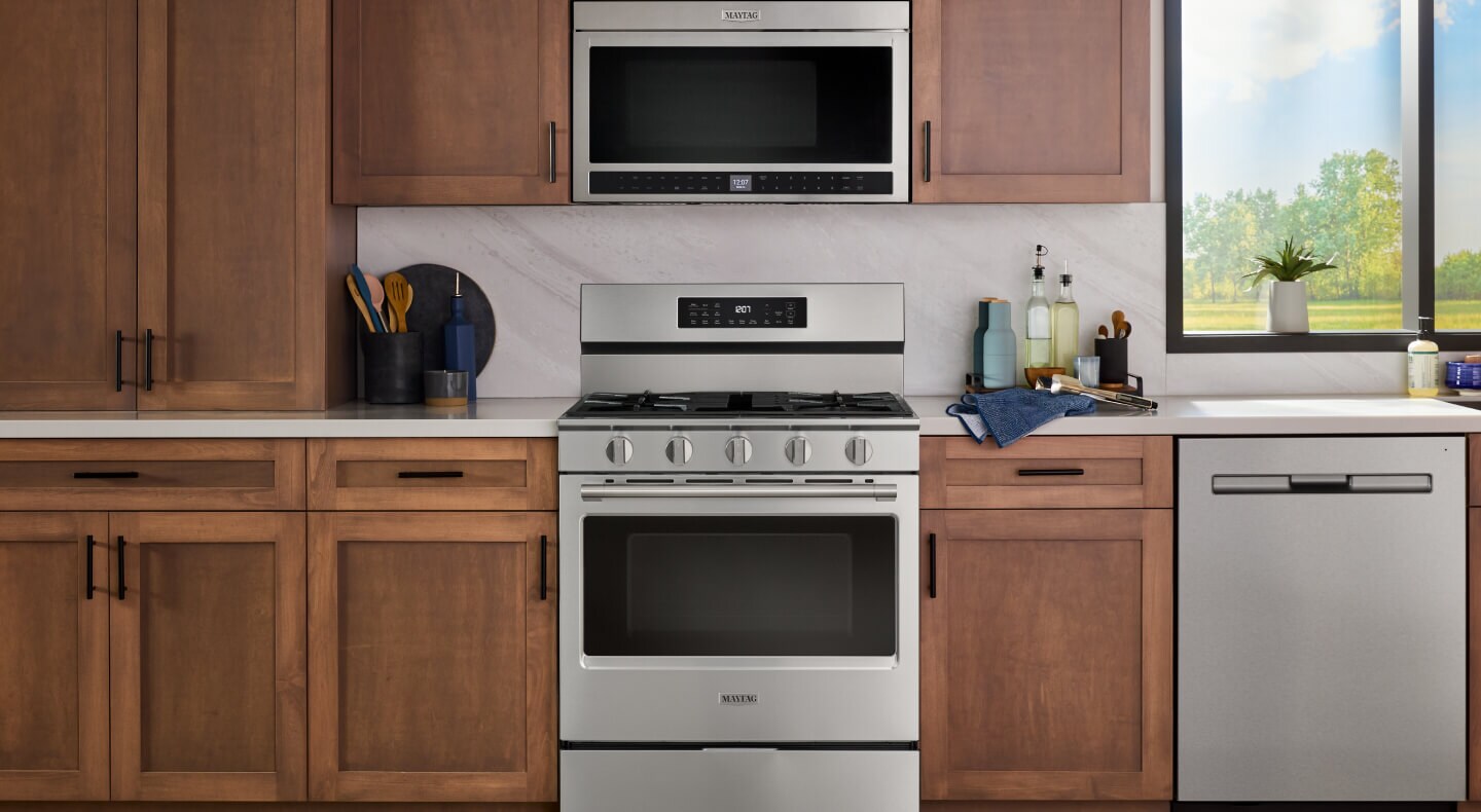 The inside of a kitchen with wooden cabinetry and a Maytag brand gas stove