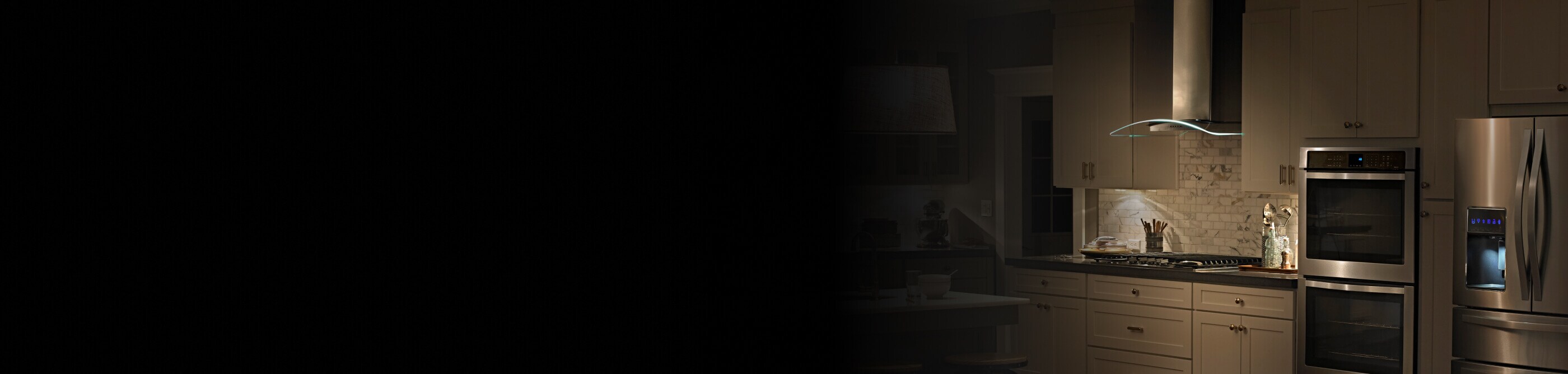 A wide view of a kitchen with a French door refrigerator, dual ovens and a wall-mount canopy hood over a cooktop