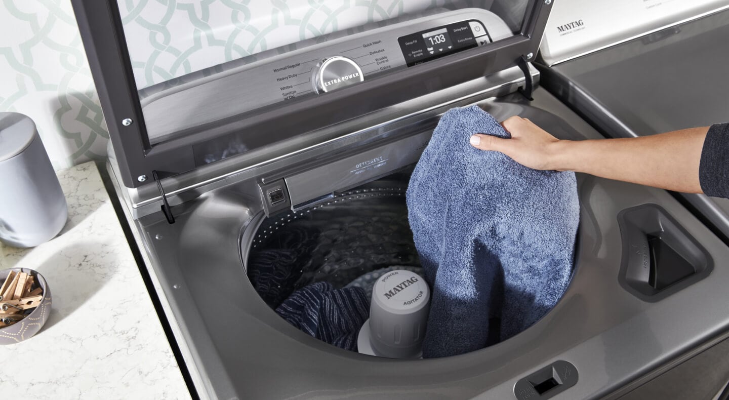 A person adding towels to a Maytag® top load washer A person adding towels to a Maytag® top load washer