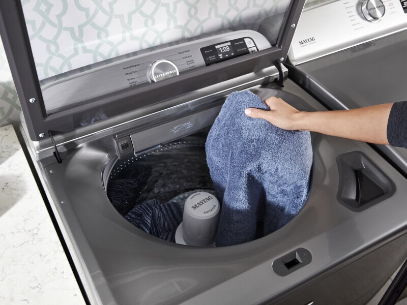 A person adding towels to a Maytag® top load washer A person adding towels to a Maytag® top load washer