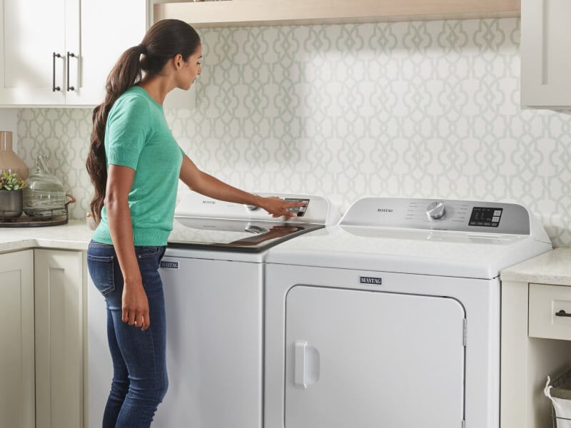 A person selecting a wash cycle on a Maytag® top load washer in modern laundry room A person selecting a wash cycle on a Maytag® top load washer in modern laundry room