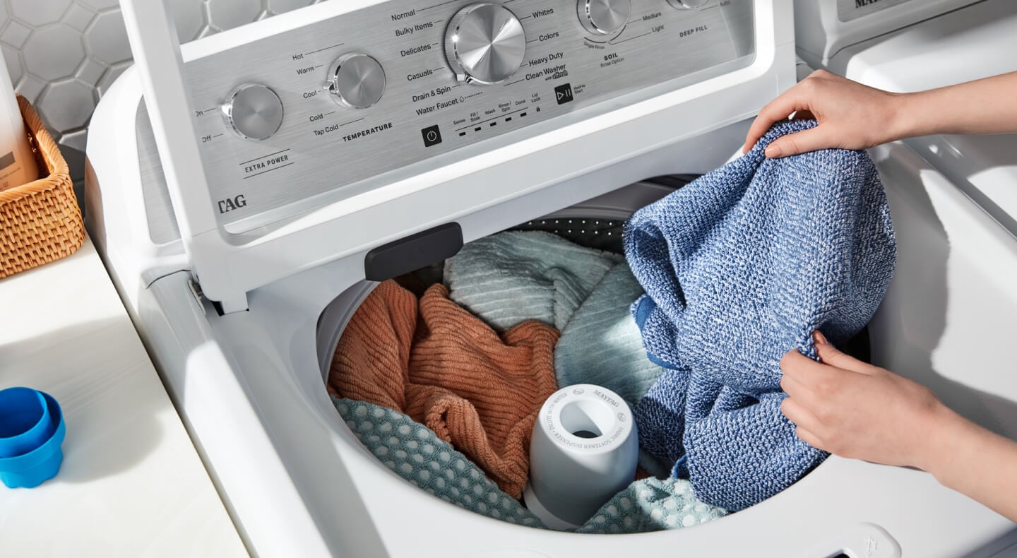 A closeup of a person adding laundry items to a Maytag® top load washer A closeup of a person adding laundry items to a Maytag® top load washer