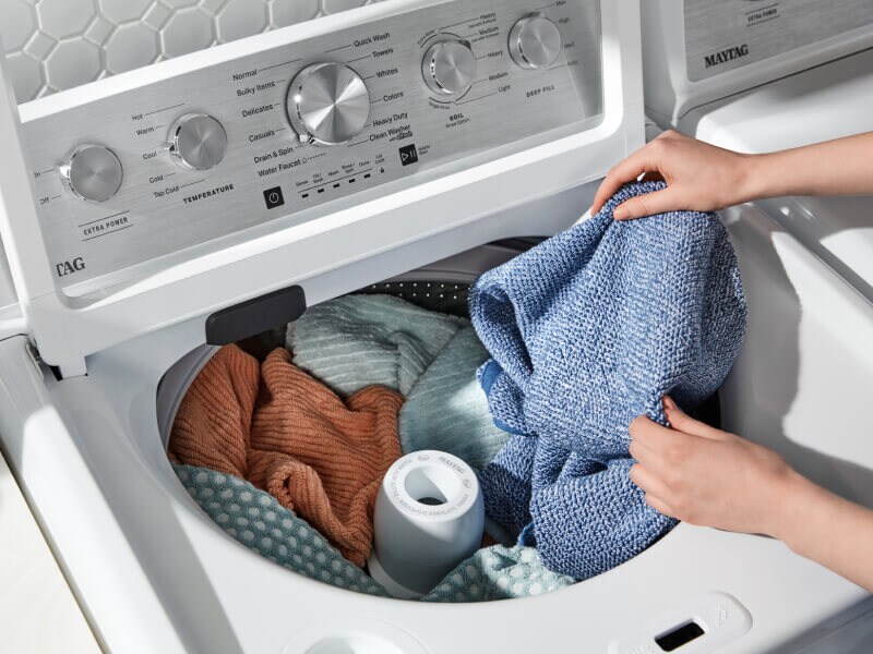 A closeup of a person adding laundry items to a Maytag® top load washer A closeup of a person adding laundry items to a Maytag® top load washer