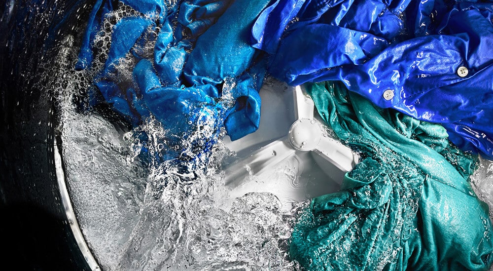 Colored clothing items spinning in water around agitator inside washing machine Colored clothing items spinning in water around agitator inside washing machine