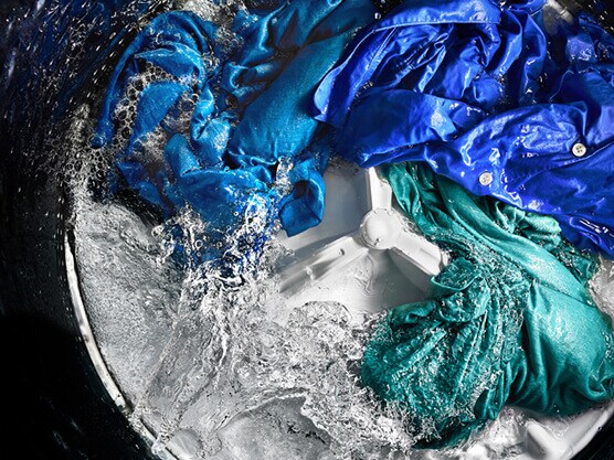 Colored clothing items spinning in water around agitator inside washing machine Colored clothing items spinning in water around agitator inside washing machine