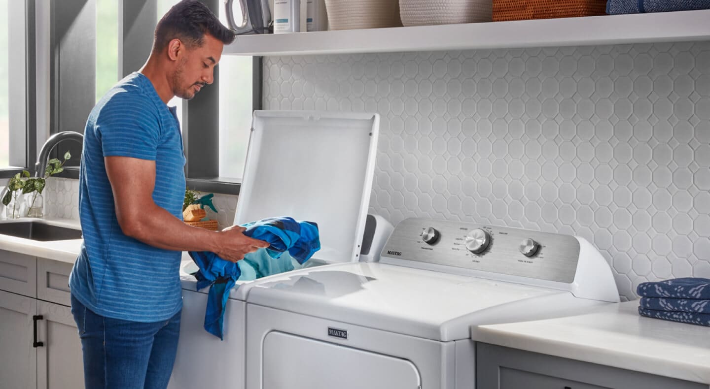 A person adding laundry items to a Maytag® top load washer in a modern laundry room A person adding laundry items to a Maytag® top load washer in a modern laundry room