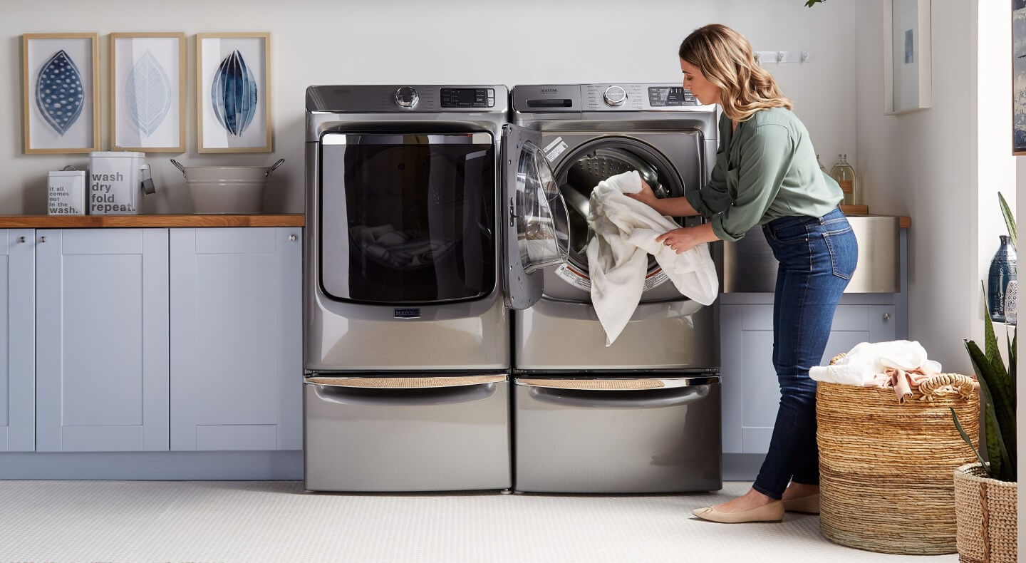 A person adding laundry items to a Maytag® dryer in modern laundry room A person adding laundry items to a Maytag® dryer in modern laundry room