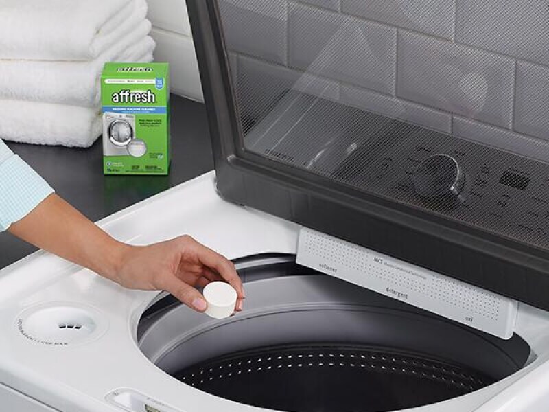 Person placing an affresh® washing machine cleaning tablet into a top load washer drum