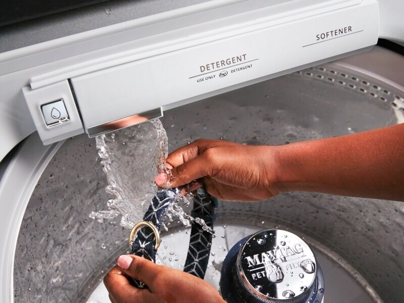 Person cleaning a belt using a Maytag® washing machine with Built-In Water Faucet