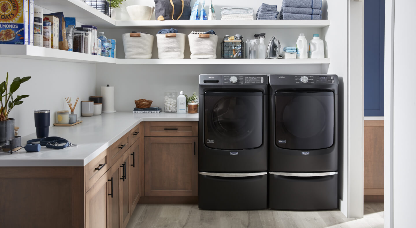 A dark, front load washer and dryer pair in a laundry room with open shelving above