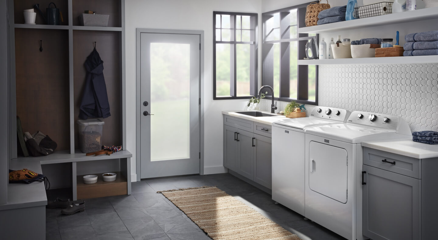 A laundry area with a white, front load washer and dryer pair with open shelving above