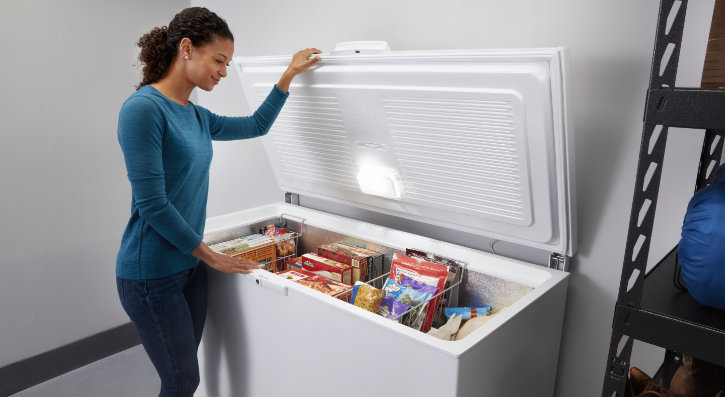 A woman opening a white chest freezer with various frozen items inside A woman opening a white chest freezer with various frozen items inside