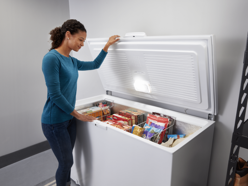 A woman opening a white chest freezer with various frozen items inside A woman opening a white chest freezer with various frozen items inside