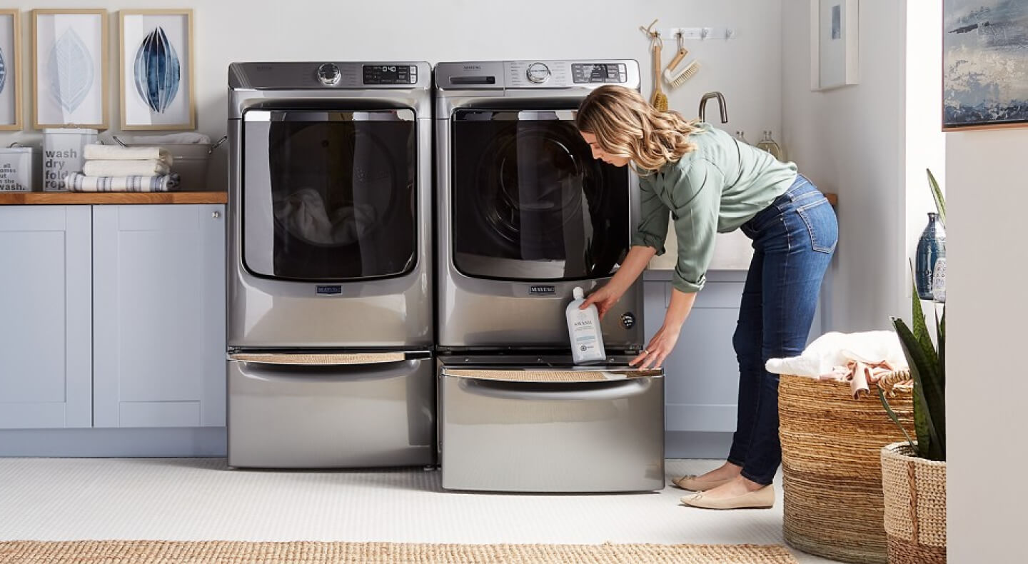 Person placing laundry supplies into an open pedestal drawer under a front load machine