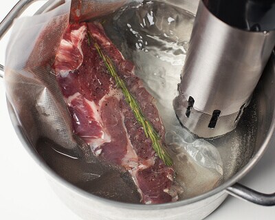 Piece of meat seasoned with rosemary in water with circulator tool in it