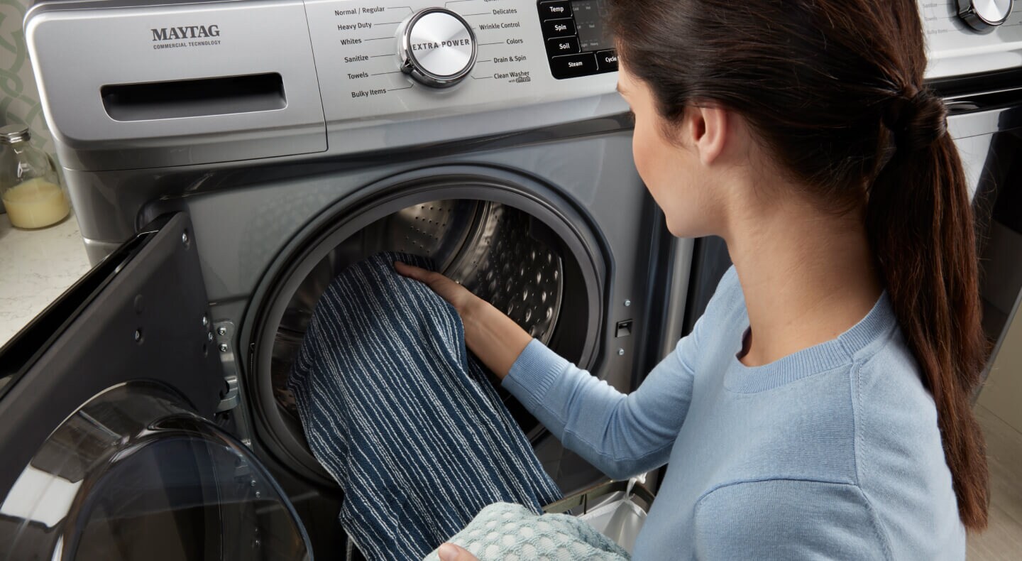 Person placing clothes inside the drum of a Maytag® front load washer