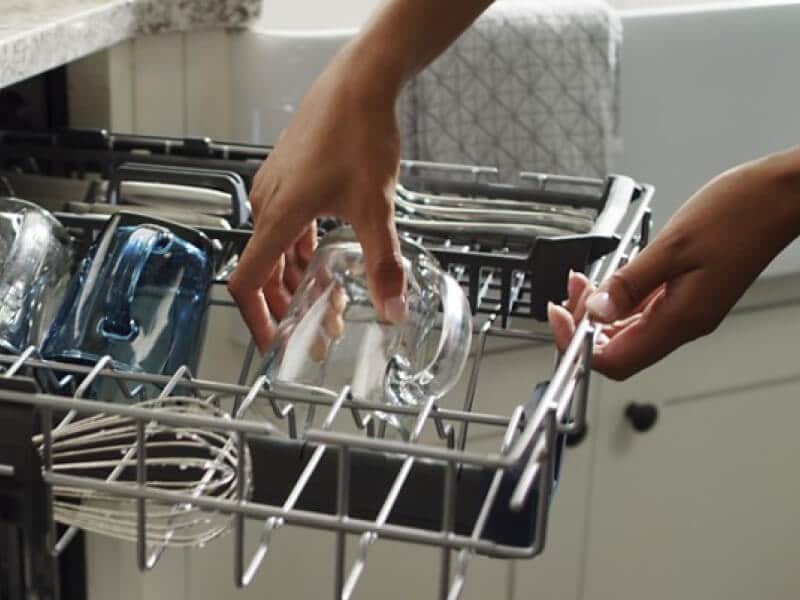 A person grabbing a glass mug out of a Maytag® dishwasher