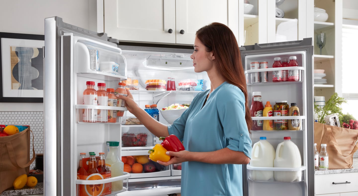 Person loading door shelves of a Maytag® French door refrigerator with beverages Person loading door shelves of a Maytag® French door refrigerator with beverages