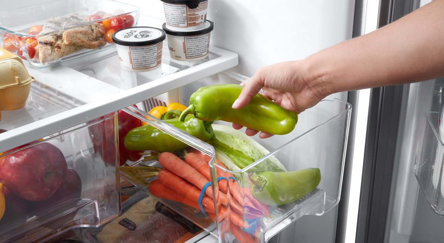 Person placing peppers into a crisper drawer Person placing peppers into a crisper drawer