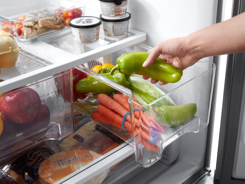 Person placing peppers into a crisper drawer Person placing peppers into a crisper drawer