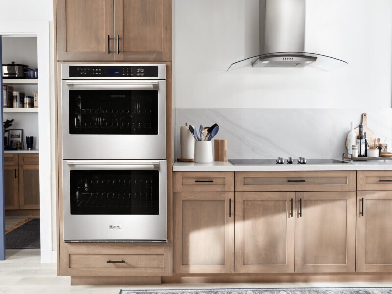 A Maytag® double wall oven, cooktop and range hood in a modern kitchen