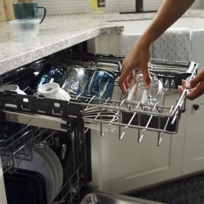 Person placing a glass mug in the top rack of a third rack dishwasher