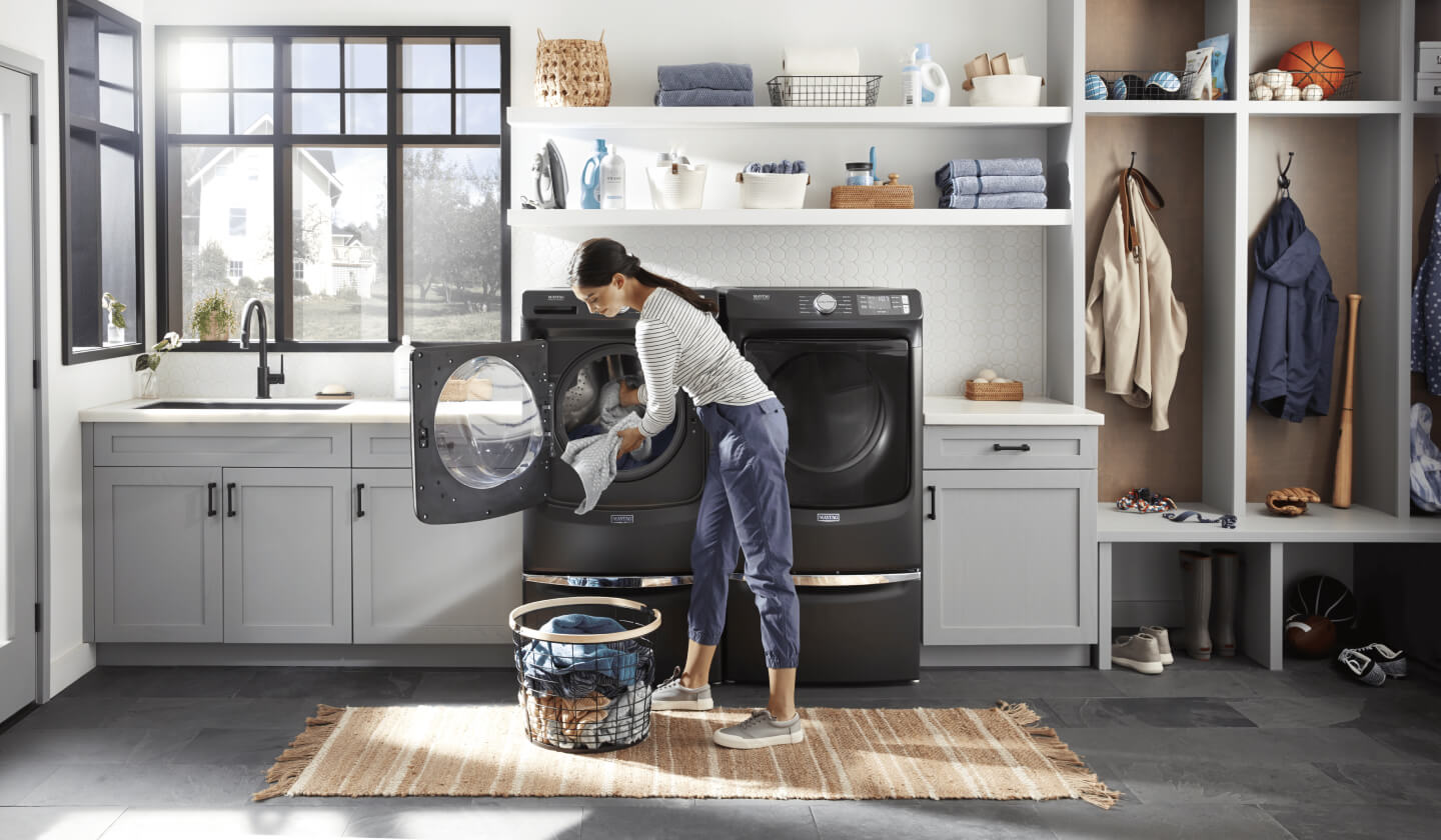 A person doing laundry with a top-load Maytag® washer and dryer set