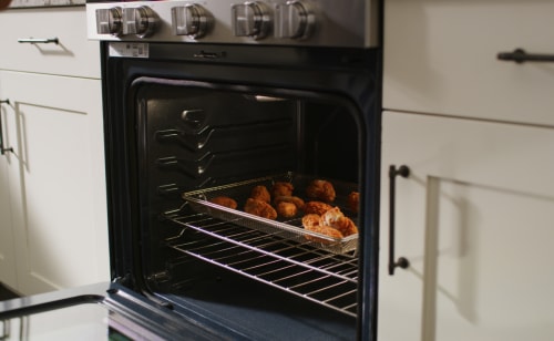 Open oven with food cooking inside of an air fry basket.