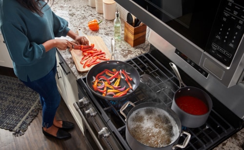 Person chopping bell peppers next to bell peppers sauteing on the stovetop