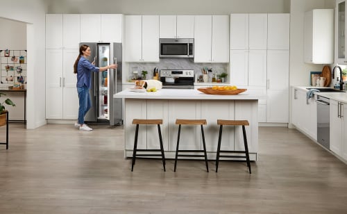 Someone opens their side-by-side fridge in a large, bright, white kitchen