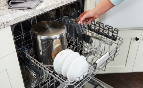 A metal stock pot and other dirty dishes loaded in a dishwasher rack