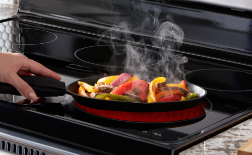 Person cooking with a skillet on a glass stovetop