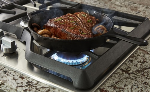 Large steak cooking with herbs on a gas cooktop