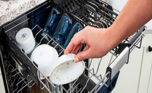 Hand placing dirty bowl in the top rack of a dishwasher