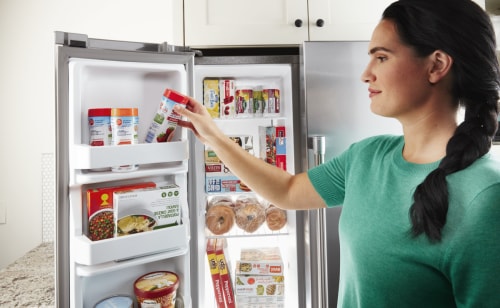 Person removing frozen food from a side-by-side fridge freezer compartment