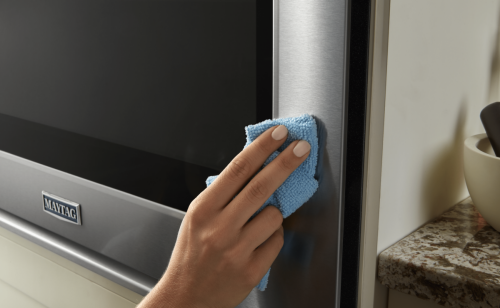 A hand holding a cloth wiping down the exterior of the oven door