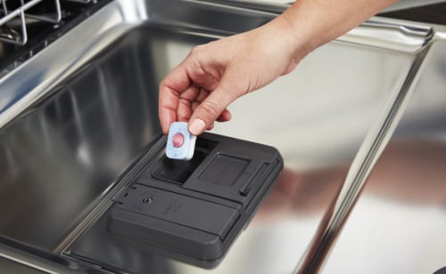 Person adding a detergent tablet to a dishwasher