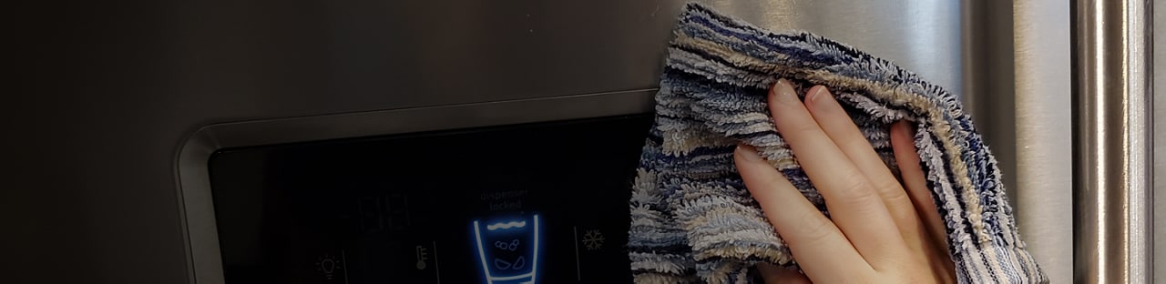 A hand cleaning the surface of a Maytag® refrigerator