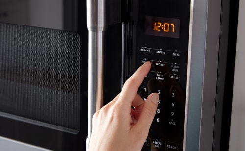 Person selecting settings on a stainless steel, over-the-range microwave control panel