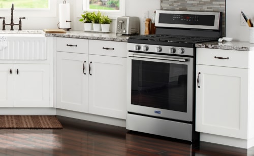 Maytag stainless steel oven set between white cabinets