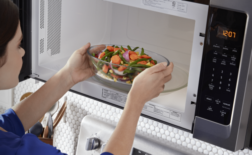 Person putting vegetables in a microwave oven