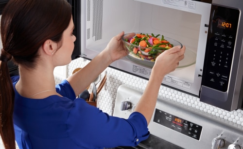 Person placing a bowl of vegetables inside a microwave