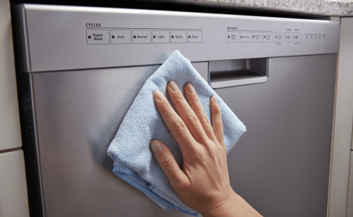Person wiping down the door panel of a stainless steel dishwasher