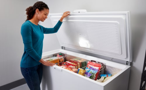 Person opening lid of a chest freezer full of frozen food