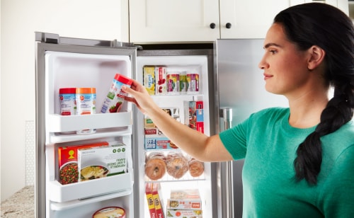 A person storing a container of fruit in a side-by-side refrigerator door
