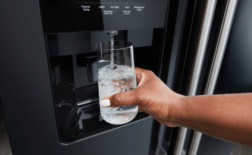 Person filling up their glass with water from a Maytag® refrigerator